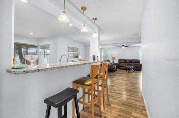 A modern kitchen with a central island, wooden bar stools, and pendant lighting.
