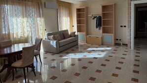 A spacious living area with a sofa, dining table, chairs, and built-in shelving. - Apartment in the heart of EUR (Roma)