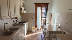 A kitchen with a gas stove, sink, cabinets, and a dining area with chairs. - Apartment in the heart of EUR (Roma)