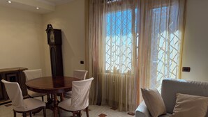 A dining area with a wooden table and chairs, a sofa, and a large window with curtains. - Apartment in the heart of EUR (Roma)