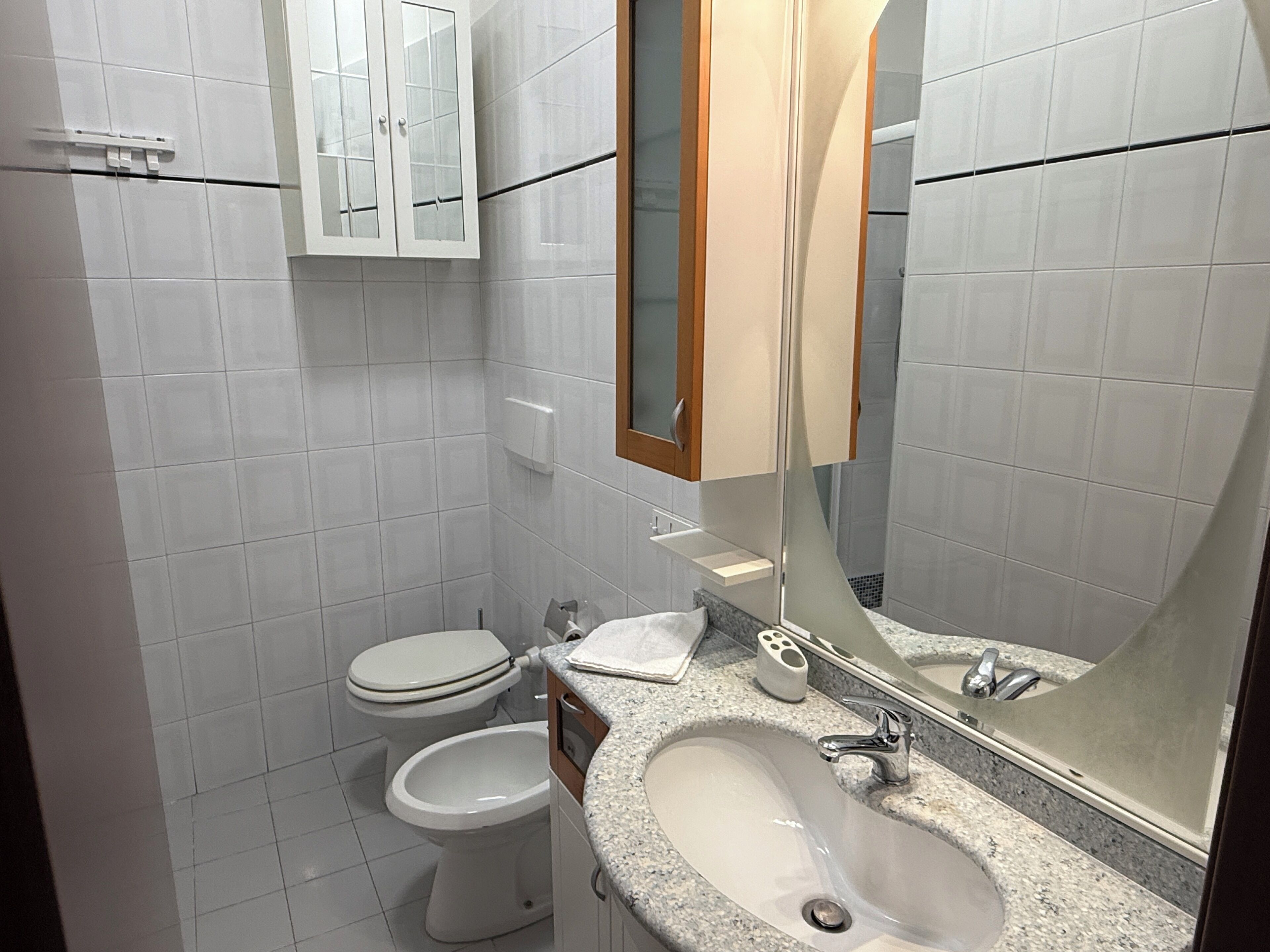 A modern bathroom with a sink, two toilets, and a mirror.