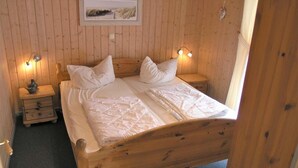Een houten bed met witte lakens in een kamer met houten wanden en een ingelijste foto aan de muur.