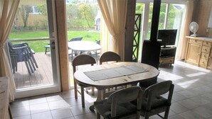 Een kamer met een eettafel en stoelen, een televisie en uitzicht op een tuin door een glazen deur.
