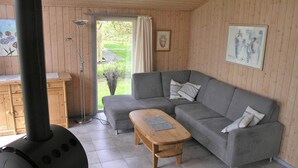 Een gezellige woonkamer met een grijze bank, een houten bijzettafeltje en een groot raam met gordijnen.
