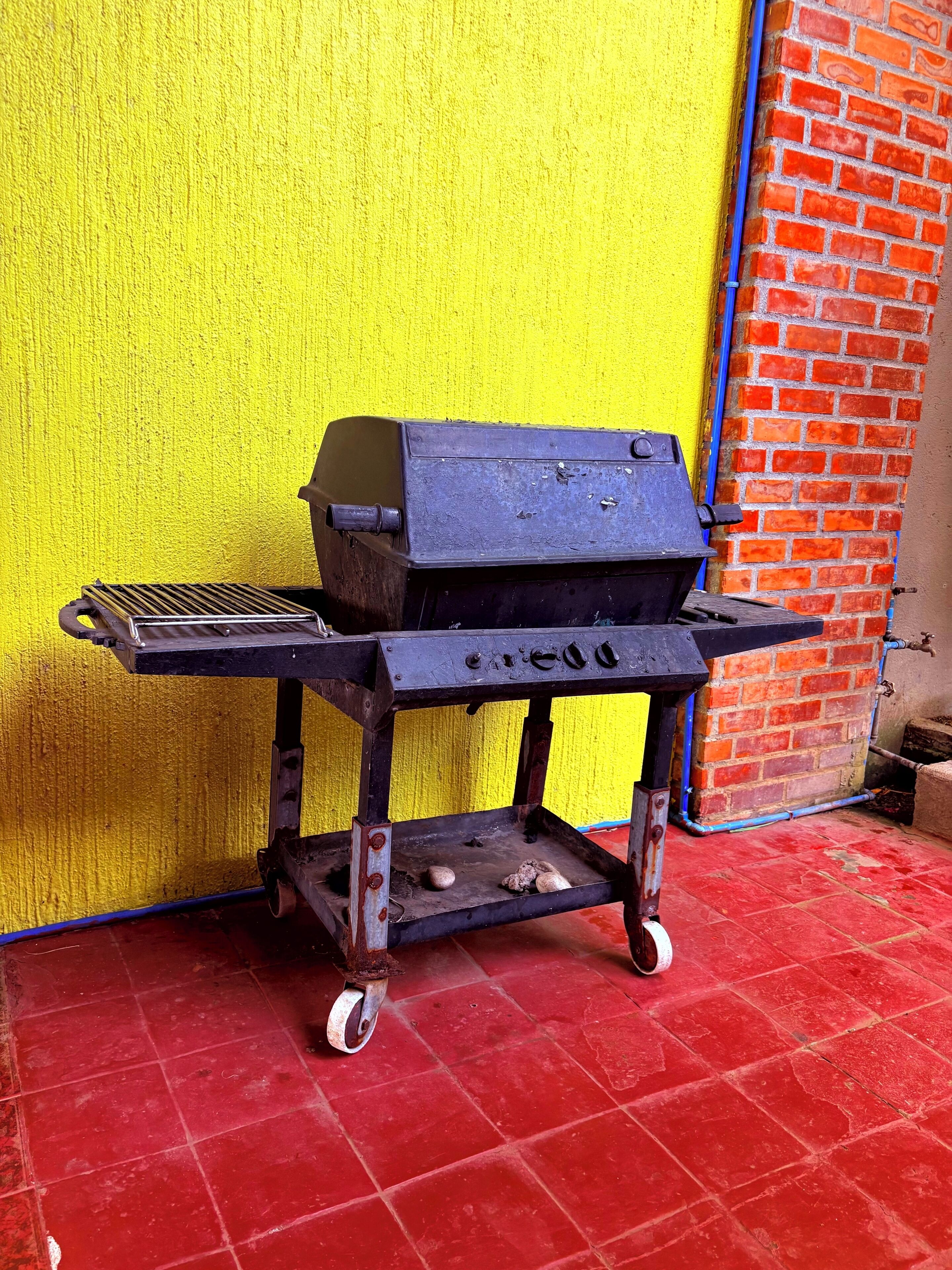 Un barbecue portatif sur roulettes, adossé à un mur jaune et à un mur en briques.
