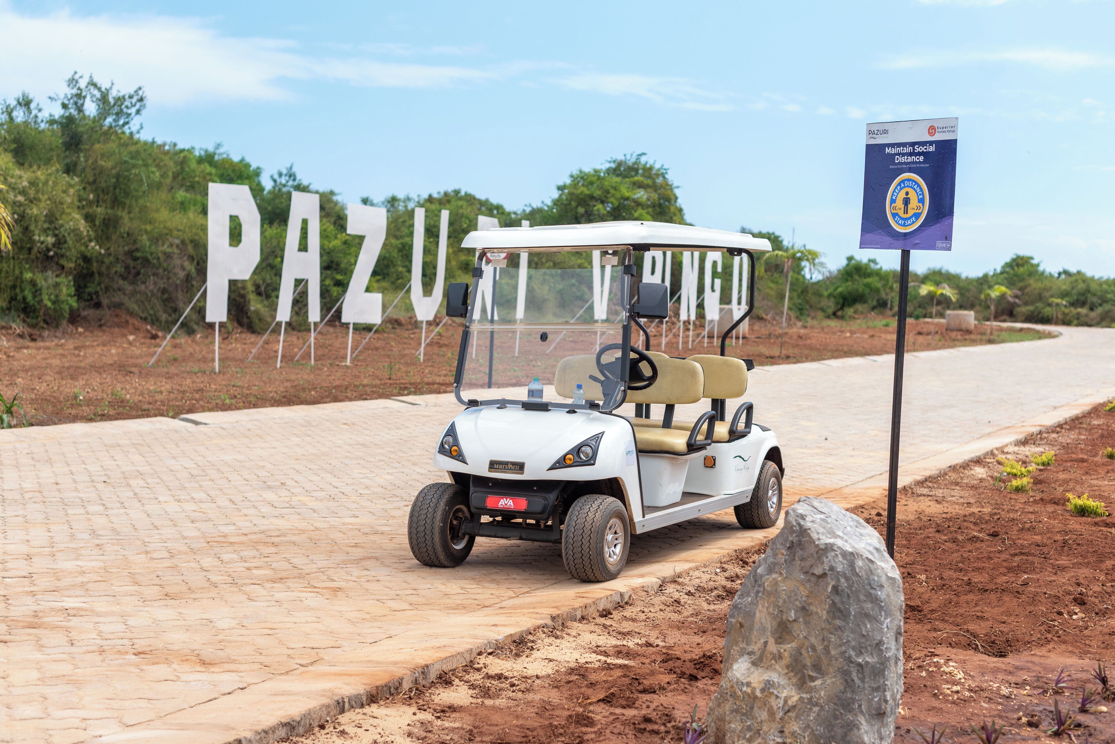 En golfbil parkerad framför en skylt med texten ”PAZU”.