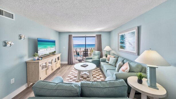 Ein Wohnzimmer mit Blick auf den Strand, inklusive Fernseher, Sofa, Couchtisch und Lampe.