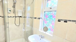Un baño moderno con ducha envuelta en vidrio, un lavamanos y un ventanal de vidrio emplomado.