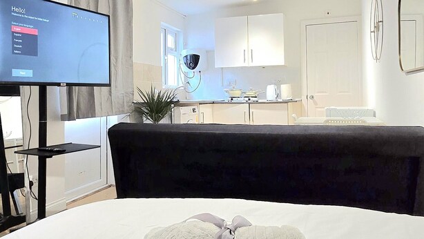 Habitación de hotel con una cama, televisión, escritorio y una kitchenette al fondo.