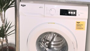 Una lavadora blanca con panel de control, una planta en maceta y paredes con azulejos color beige.