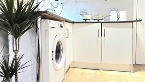 Una cocina moderna con armarios blancos, lavadora y una planta en maceta.