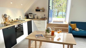 A modern kitchen with a dining area, featuring a coffee machine, kettle, and a book on the table. - Sous Le Phare (Louannec)