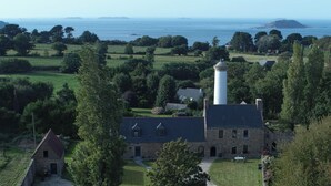 A historic building with a lighthouse, surrounded by lush greenery and a view of the sea. - Sous Le Phare (Louannec)