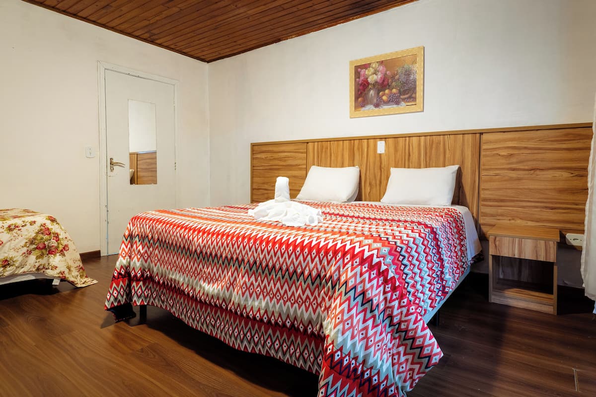 Un dormitorio con cabecera de madera, cama con colcha estampada, mesita de noche y un cuadro en la pared.