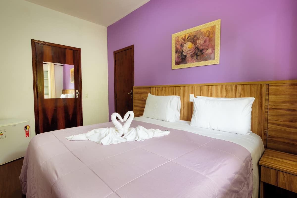 Una habitación de hotel con cama, cabecera de madera y un cuadro en la pared.