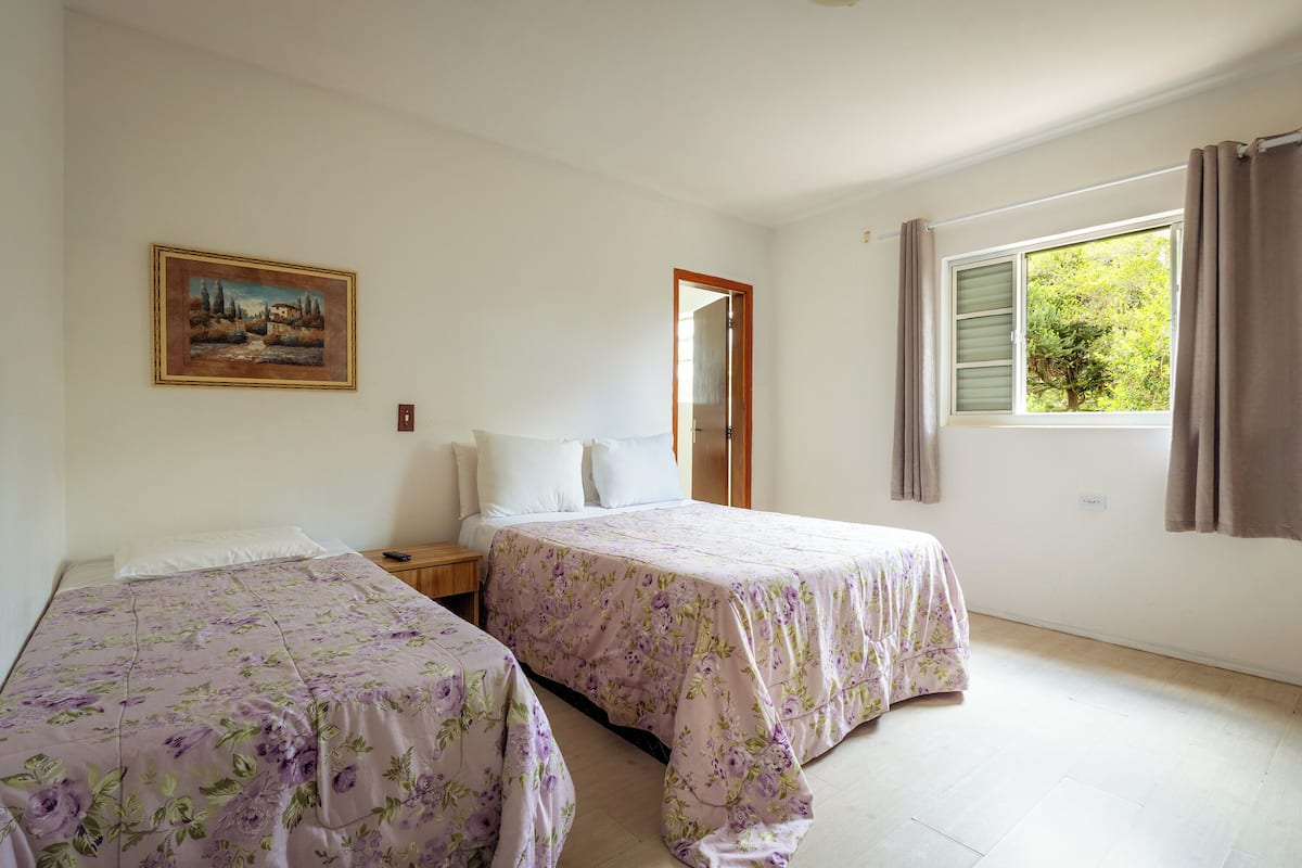 Una habitación con dos camas, un cuadro en la pared, una ventana con cortinas y una puerta.