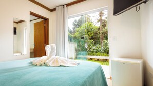 Un dormitorio con una cama, un espejo, un ventanal con vistas a la vegetación y un electrodoméstico blanco.