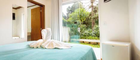 A bedroom with a bed, a mirror, a window with a view of greenery, and a white appliance.