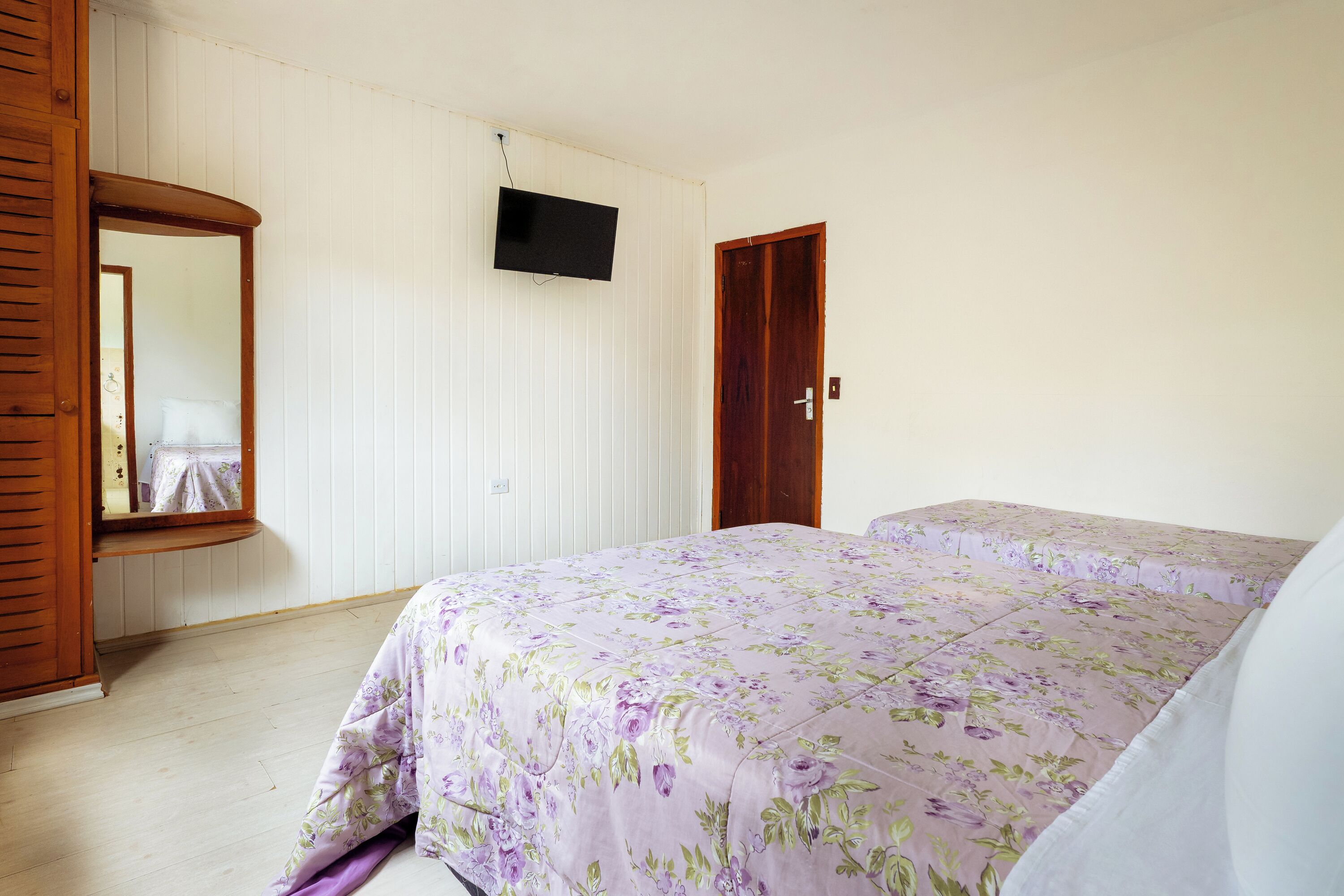 A bedroom with a bed, a wooden wardrobe, a television on the wall, and a door.