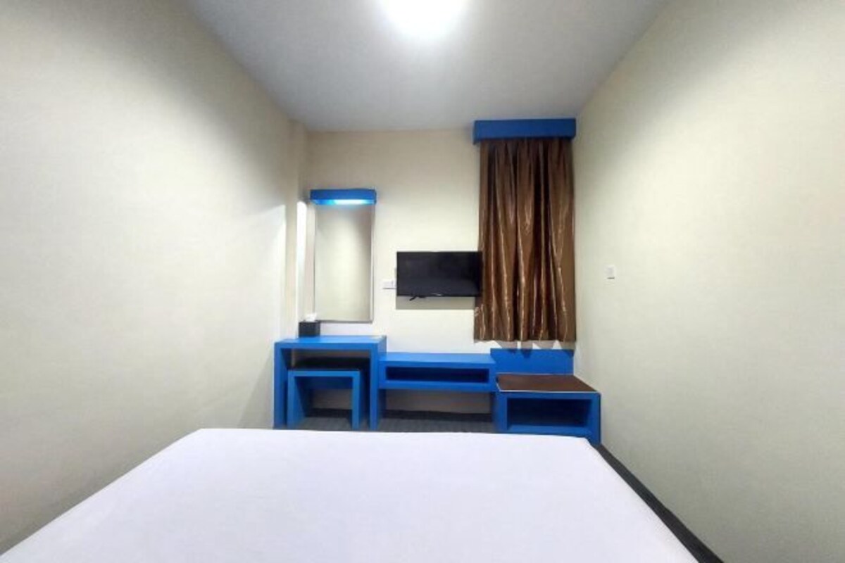 Ein Hotelzimmer mit Bett, Schreibtisch, Stuhl, Fernseher und einem Fenster mit Vorhängen.