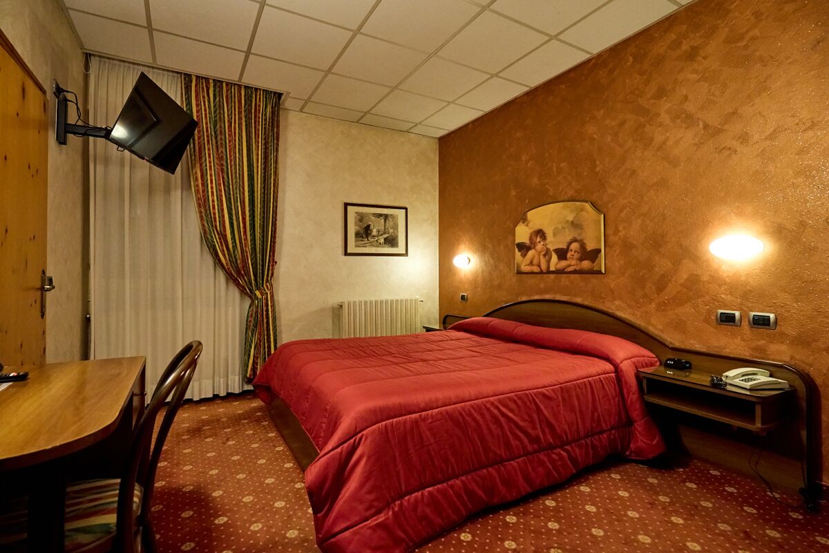 Una camera d'albergo con un letto, una scrivania, una sedia, una TV a parete e un quadro appeso al muro.
