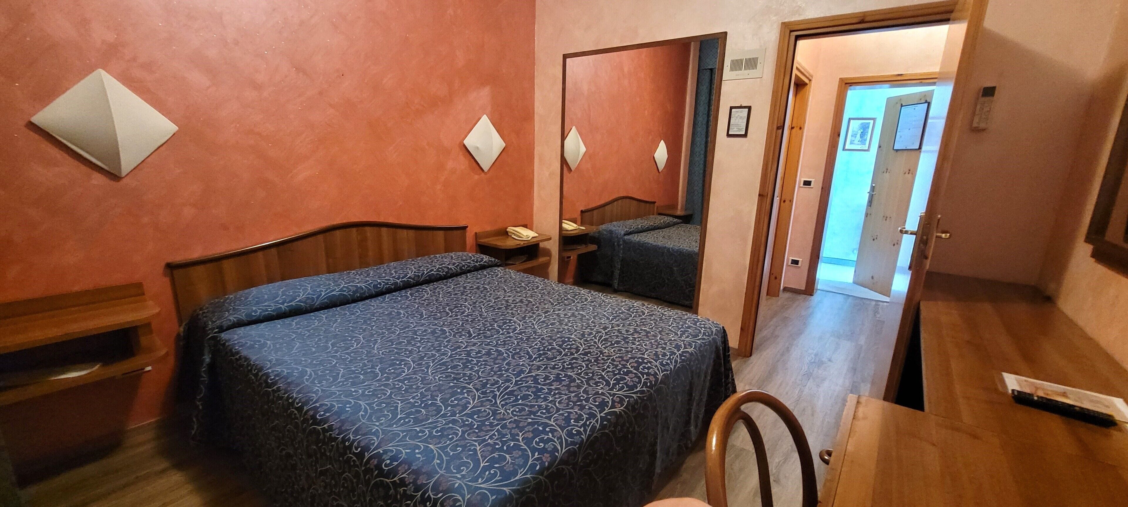 Ein Hotelzimmer mit einem großen Bett, einem Nachttisch, einem Sessel und einer Holzkommode.
