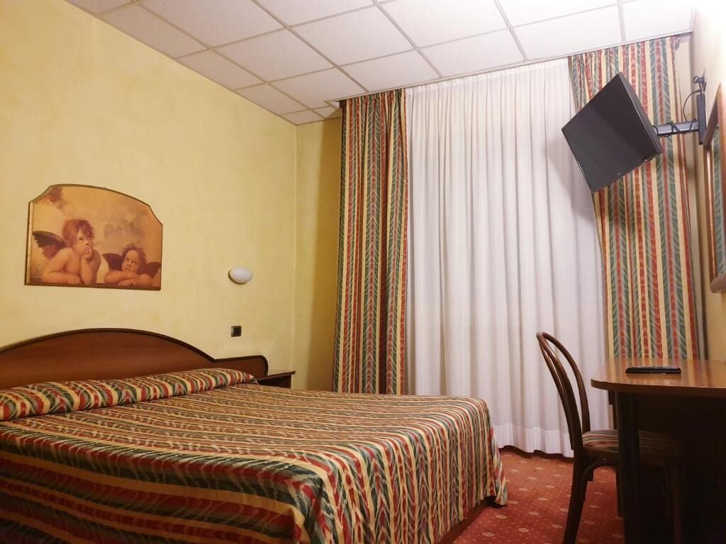 Ein Hotelzimmer mit einem Bett, einem Schreibtisch, einem Sessel, einem an der Wand befestigten Fernseher und einem Vorhang mit Streifenmuster.