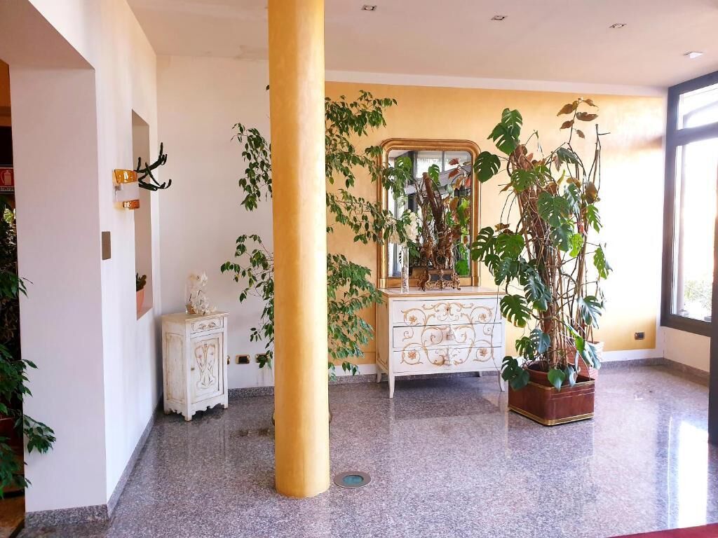 A hotel lobby with a large pillar, a white ornate dresser, and several potted plants.