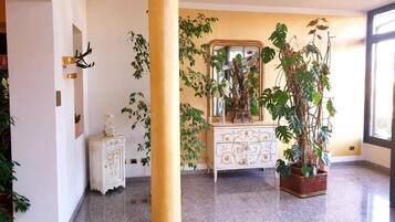A hotel lobby with a large pillar, a white ornate dresser, and several potted plants.