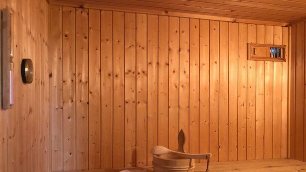 Un sauna de madera con un banco, un cubo y toallas.