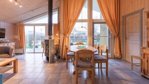 A wooden interior with a dining table, chairs, a fireplace, and large windows. - Ferienhaus im Ferienpark Mueritz (Rechlin)