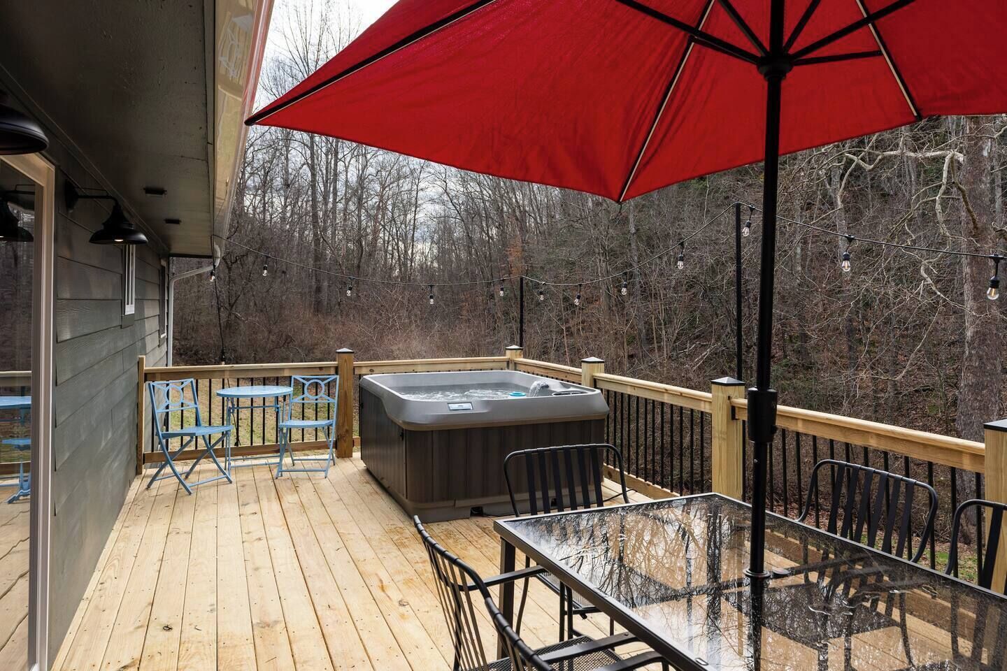 Una terraza de madera con un jacuzzi, mobiliario exterior y un paraguas rojo.