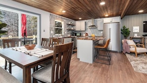 Une cuisine moderne avec un plafond en bois, un coin repas doté d’une grande table et de chaises, et un petit îlot central avec des sièges.