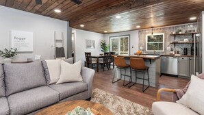 Une cuisine moderne dotée d’un îlot central, d’un plafond en bois et d’un coin repas avec un canapé et des chaises gris.