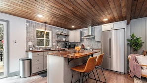 Une cuisine moderne avec un plafond en bois, un îlot central doté de tabourets de bar et un réfrigérateur en acier inoxydable.