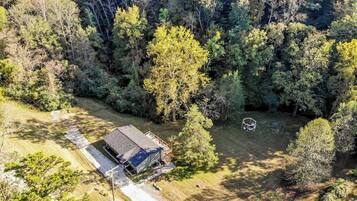 An aerial view of a property with a large barn-like structure, surrounded by dense forest.
