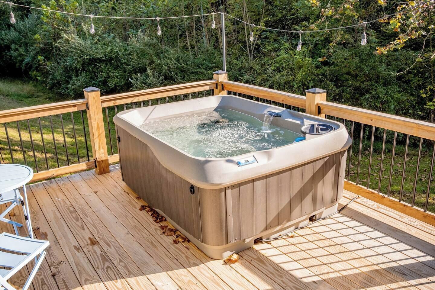 Un bain à remous sur une terrasse en bois, avec une rambarde en métal, entouré de verdure.