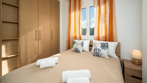 A bedroom with a large wardrobe, a bed with multiple pillows, and a nightstand with a lamp. - Levanta Cozy Apartment 3 in Kalavarda Rhodes (Rhodes)