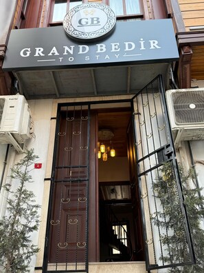 Exterior del hotel Grand Bedir, con un llamativo letrero, una puerta de entrada decorativa y unidades de aire acondicionado en la fachada.