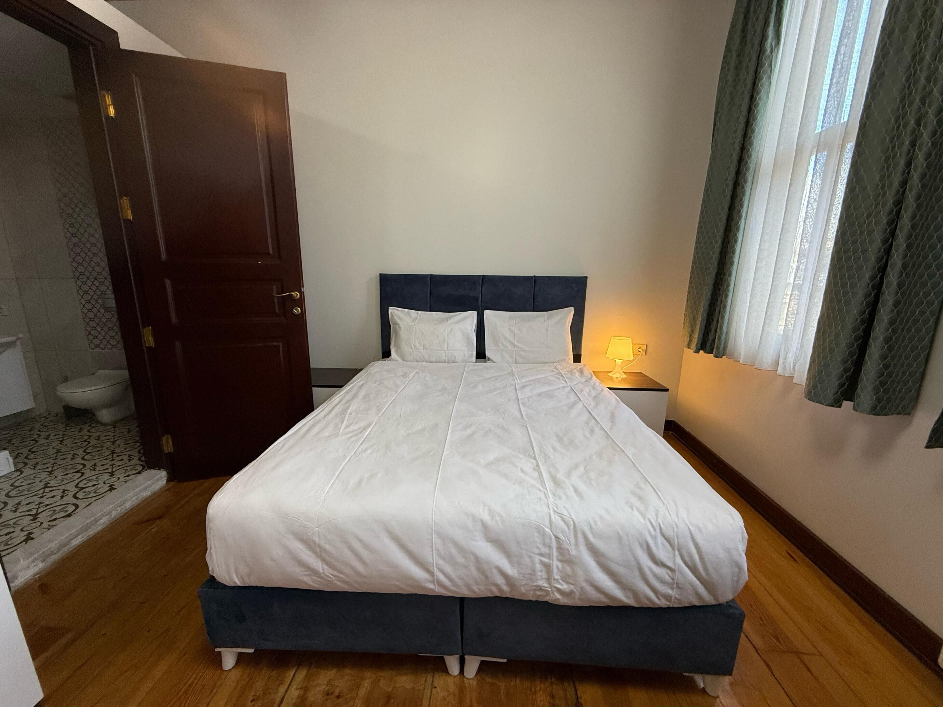Una cama bien hecha con ropa blanca, un cabecero oscuro y una lámpara de noche.