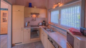 A compact kitchen with wooden cabinets, a built-in oven, a sink, and a window with curtains. - Ferienhaus im Skandinavischen Stil (Rechlin)