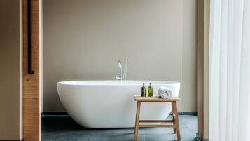 A modern bathroom with a freestanding bathtub, a wooden stool, and two bottles of liquid soap.