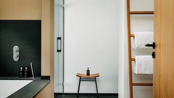 Un baño moderno con encimera negra, un taburete de madera, cabina de ducha de vidrio y un perchero de madera.