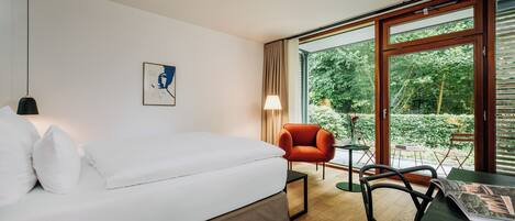 Une chambre d’hôtel moderne, équipée d’un lit, d’un bureau, d’une chaise, d’une lampe et d’une fenêtre donnant sur un paysage verdoyant.