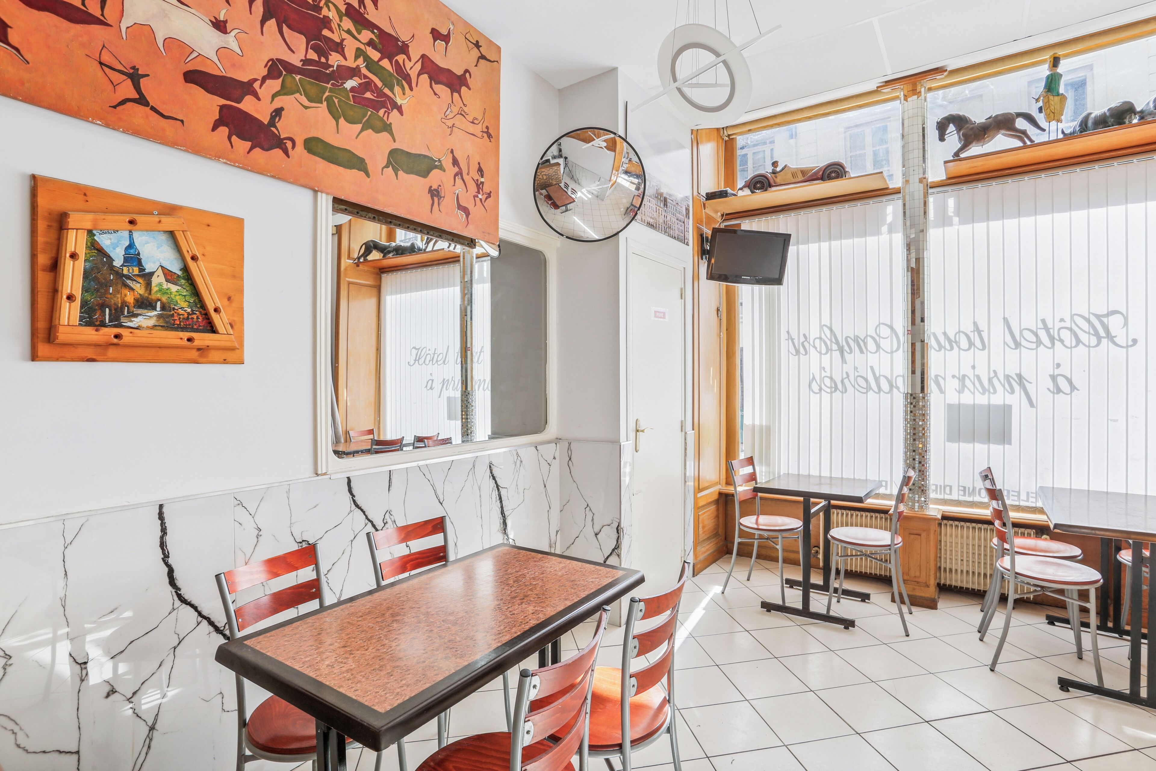 A dining area with a marble floor, wooden chairs, and a table. There are decorative elements on the walls, including a painting and a mirror.