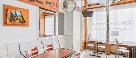Un comedor con piso de mármol, sillas de madera y una mesa. Hay elementos decorativos en las paredes, como un cuadro y un espejo.