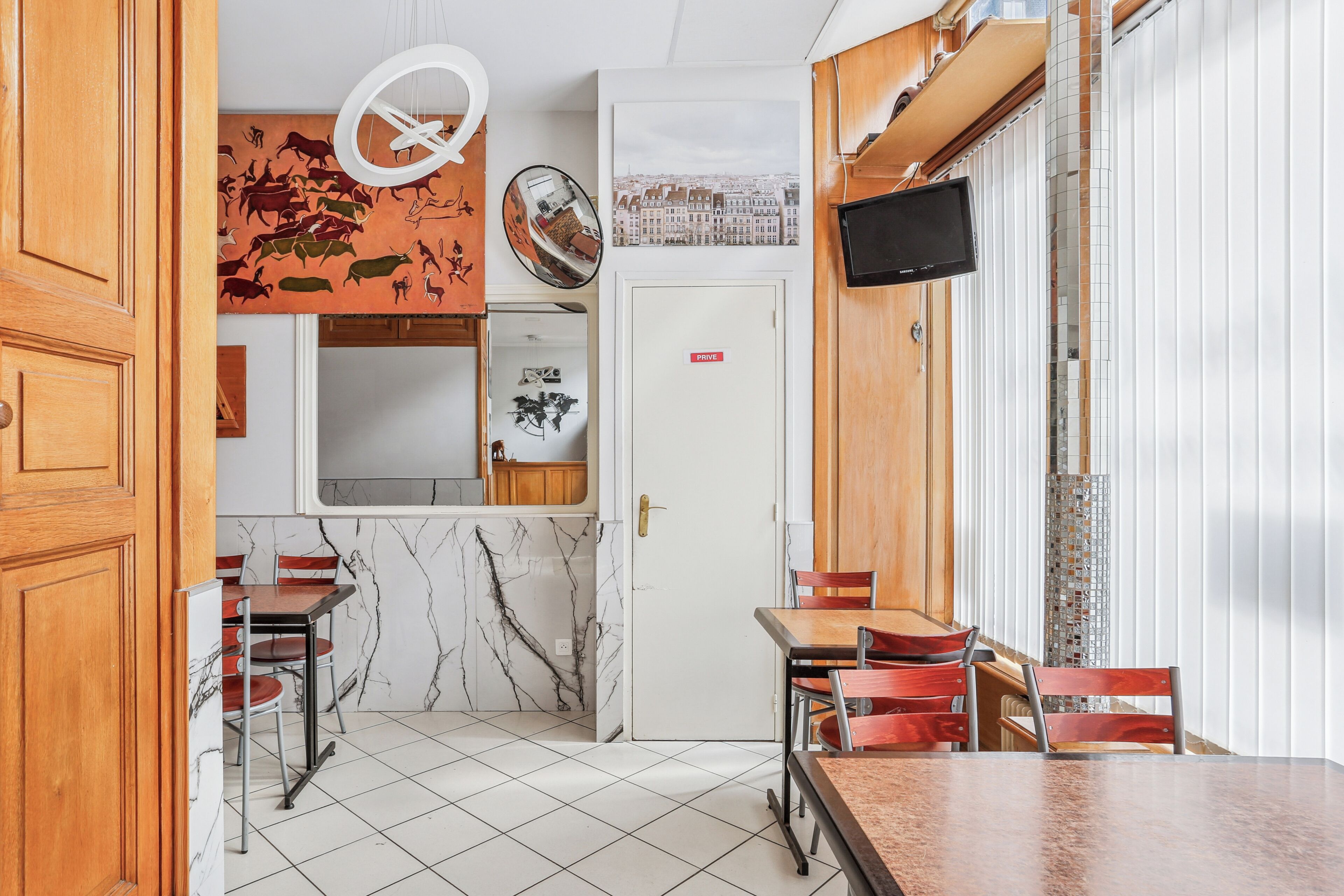 A restaurant with marble flooring, wooden furniture, a white door with a 'PRIVATE' sign, and a cityscape poster.