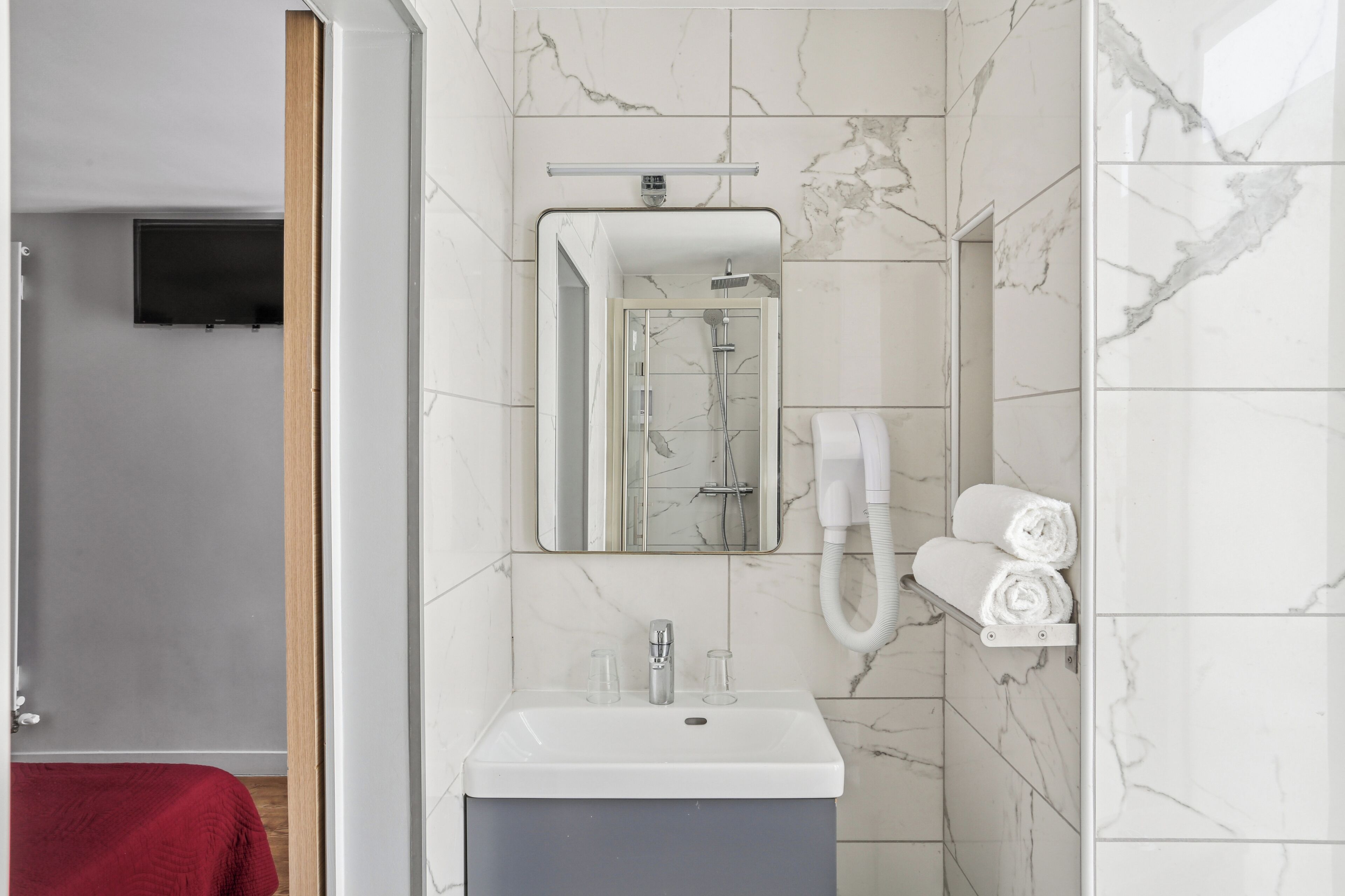 Ein modernes Badezimmer mit einer Dusche mit Marmorplatten, einem Waschbecken und einem Spiegel.