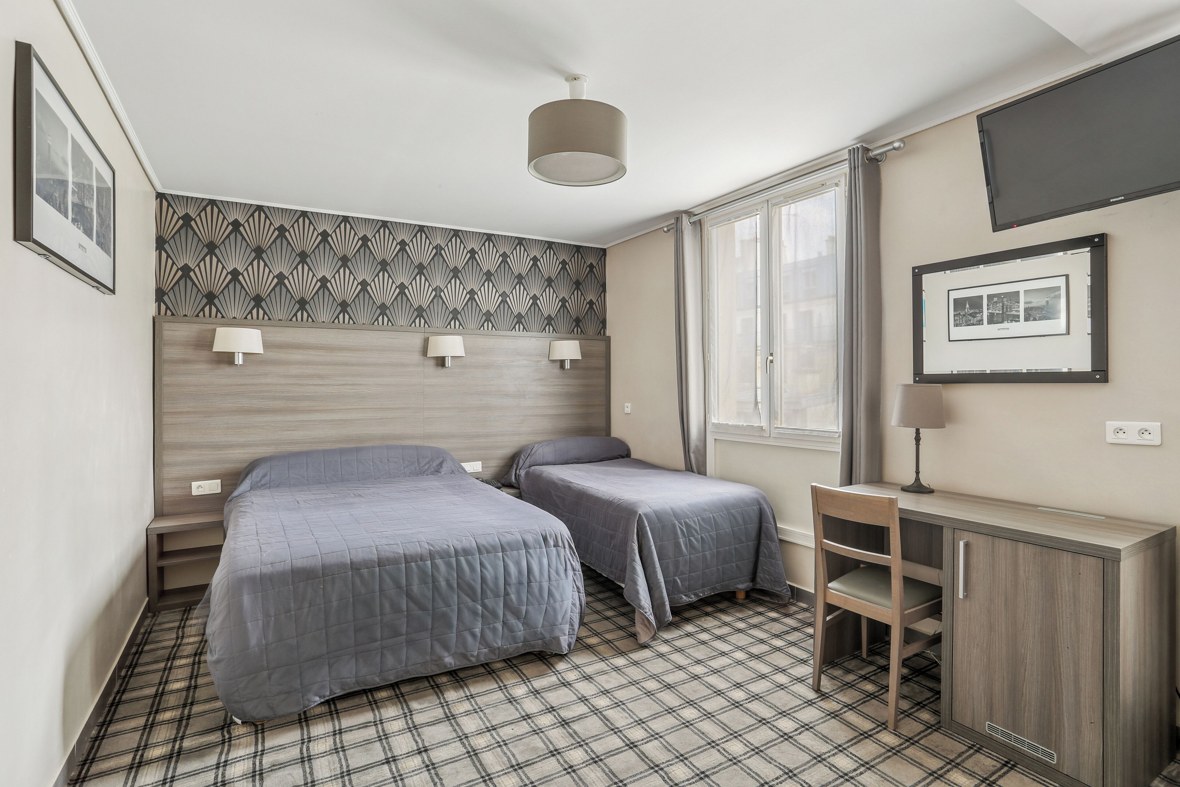 A room with two beds, a desk, a chair, a TV, and a patterned wall.