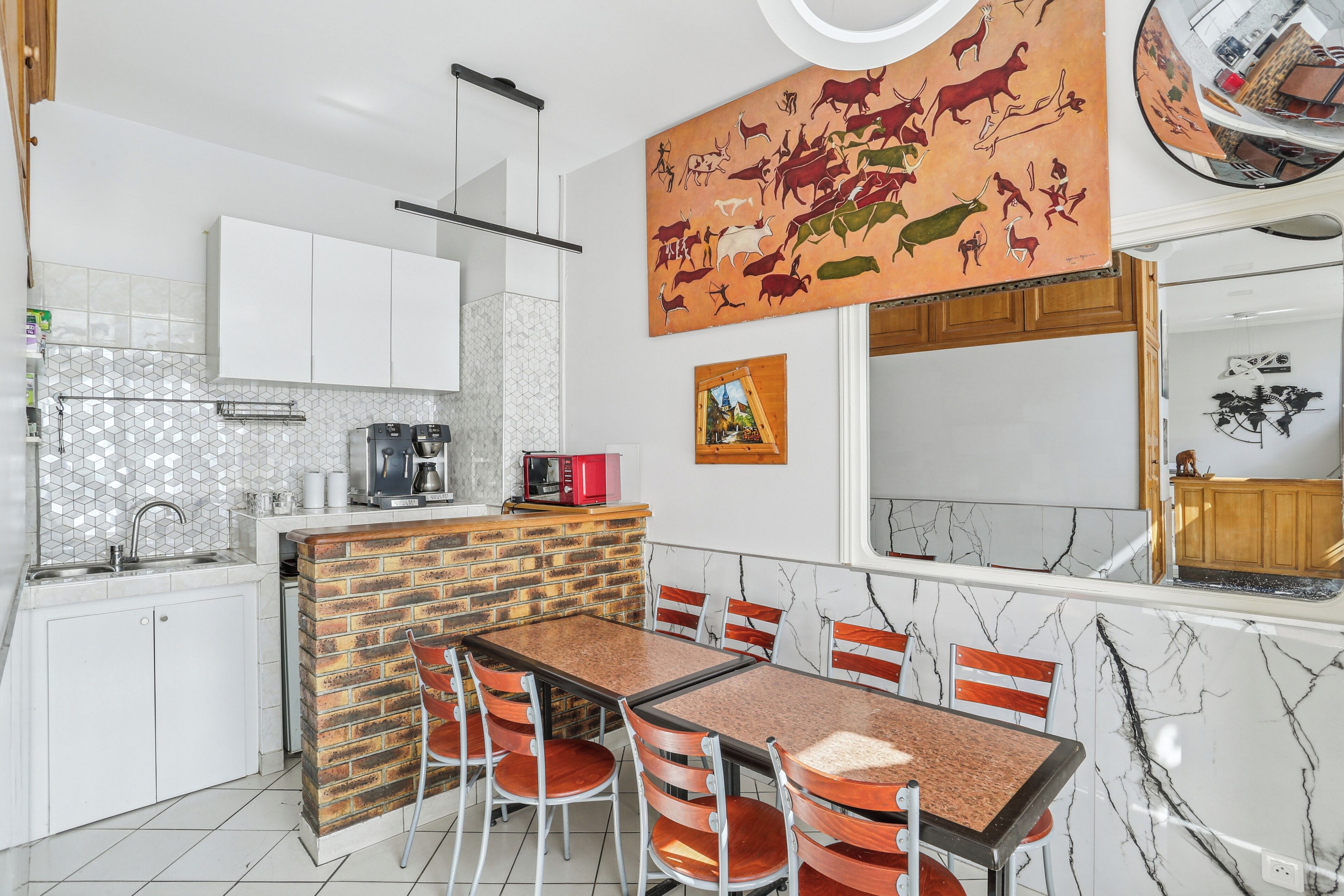 Una cocina moderna con armarios blancos, una pared de acento de ladrillo, una zona de comedor con encimera de mármol y un gran mural.